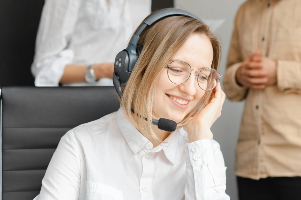 pexels-photo-7682204-7682204 A cheerful woman working at a call center, wearing a headset and glasses, providing excellent customer support.