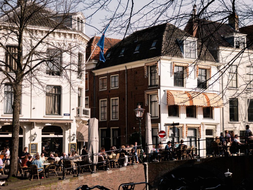 A bustling outdoor cafe in Leiden with people enjoying sunny weather by the canal.